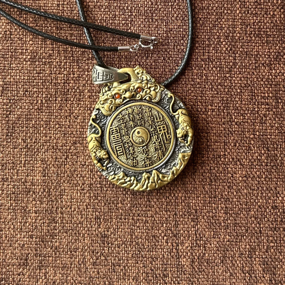 Mountain Spirit Yin Yang Bagua necklace displayed on brown fabric with its cord
